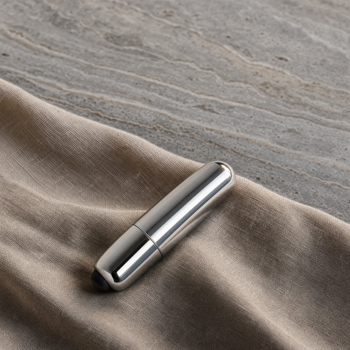 Mini balle vibrante argent sur du lin, fond travertin gris