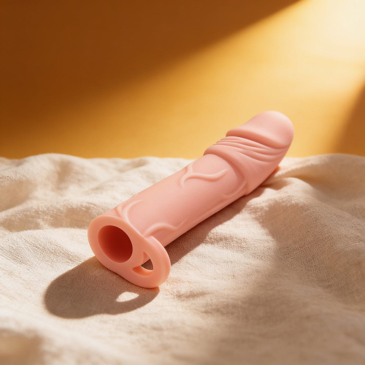 Gaine de pénis Extender Hugy Real Body — posée sur du lin drapé, lumière chaude