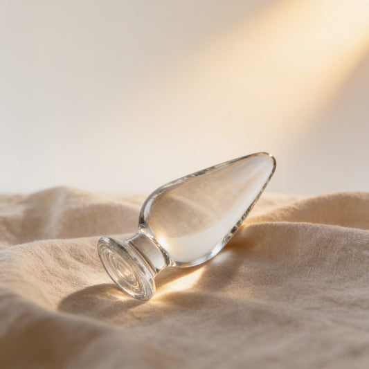 Plug anal allongé Glossy Toys transparent — posé sur du lin drapé, lumière chaude